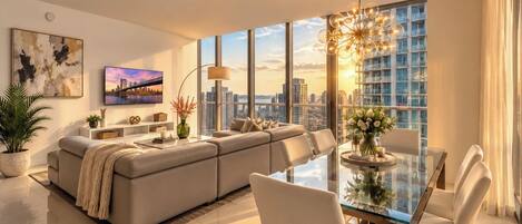 A modern living room with a sofa, a glass dining table, and a large window with a city view.