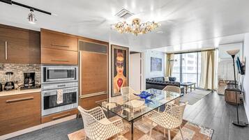 A modern kitchen with a glass dining table, white chairs, and a chandelier.
