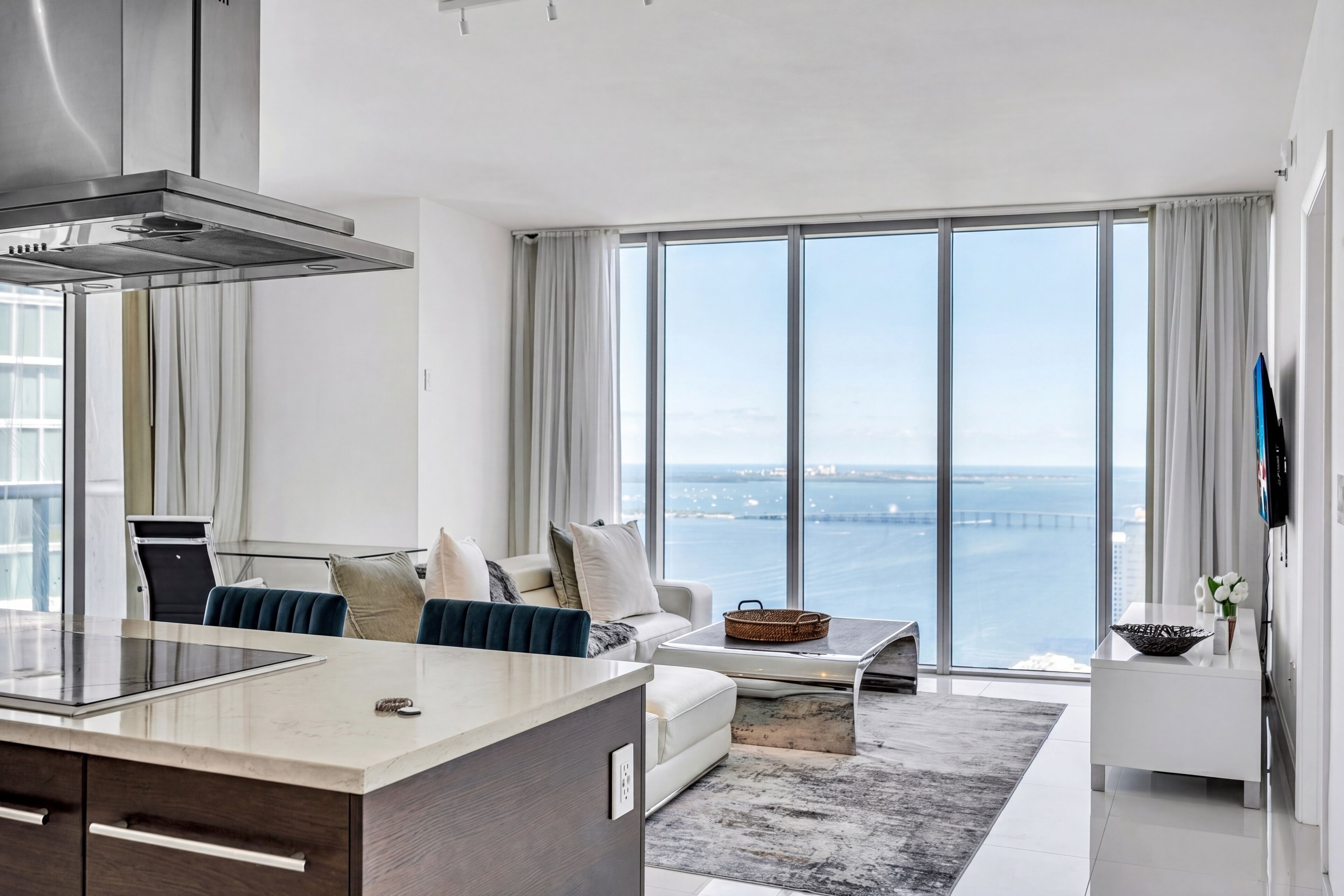 A modern living room with a large window, a kitchen area, and a view of the sea.