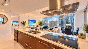 A modern kitchen with a large island, stainless steel appliances, and a view of a cityscape through large windows. - Icon Brickell  (Miami)