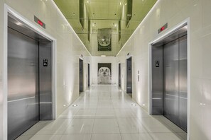 A modern elevator lobby with metallic elevator doors, a marble wall at the end, and a green-tiled ceiling. - Icon Brickell  (Miami)