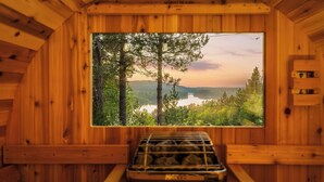 A wooden cabin interior with a large window overlooking a forest and lake.