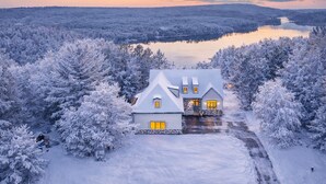 Ett snötäckt hus med en stor uppfart och en sjö i bakgrunden.
