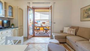 Een compacte woonruimte met kitchenette, een eethoek met tafel en stoelen, een bank en een glazen schuifdeur naar een terras.