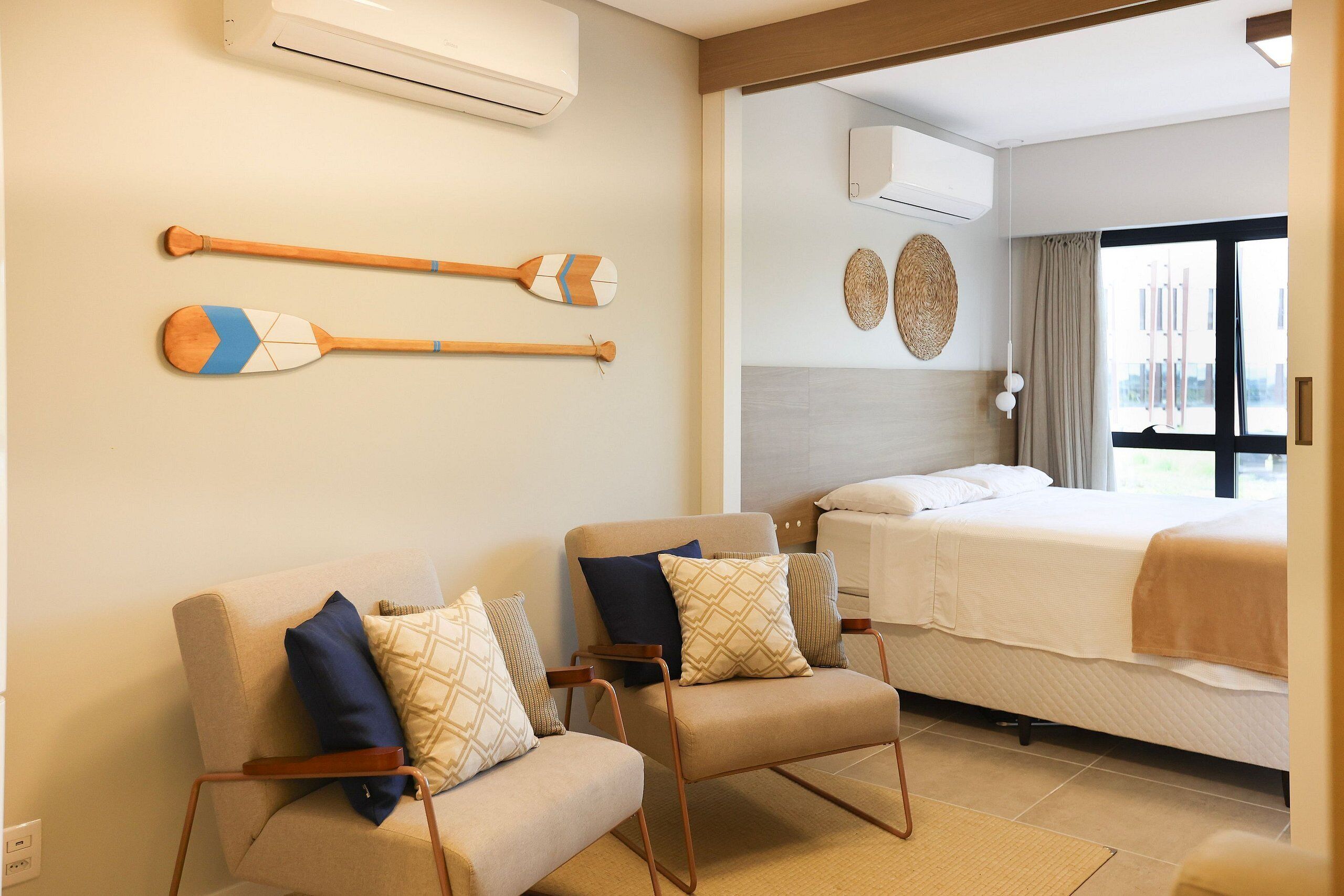 A hotel room with two armchairs, a bed, and a view of the outside.