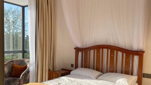 Ein Schlafzimmer mit einem hölzernen Bett, einem Nachttisch, einem Sessel und einem Fenster mit Vorhängen.