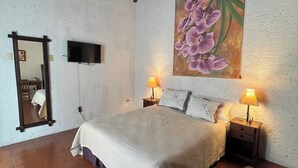 Ein Schlafzimmer mit einem Bett, zwei Nachttischlampen, einem Fernseher, einem Gemälde und einem Spiegel.