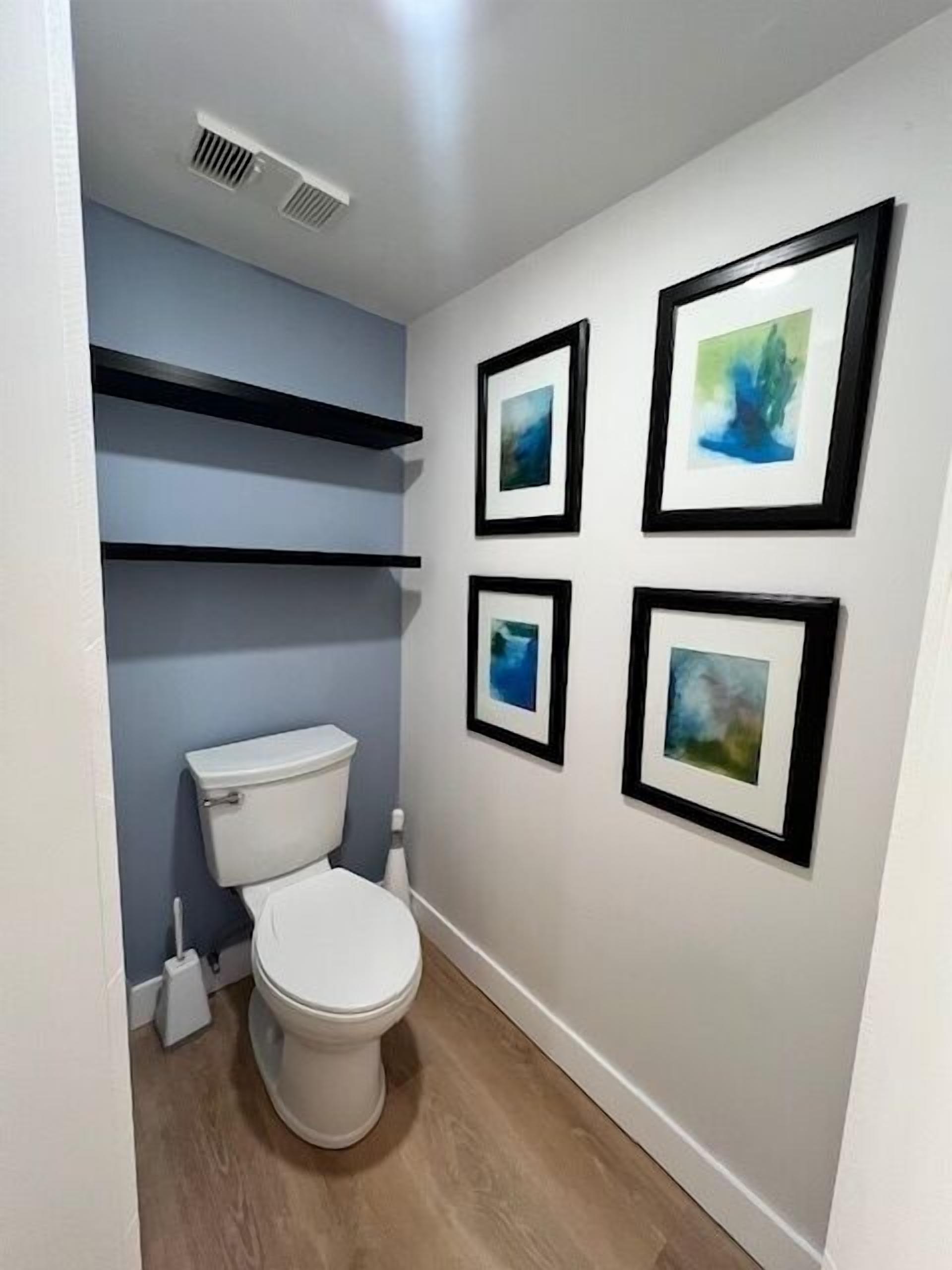 A bathroom with a toilet, a shower, and a sink. There are three framed pictures on the wall.