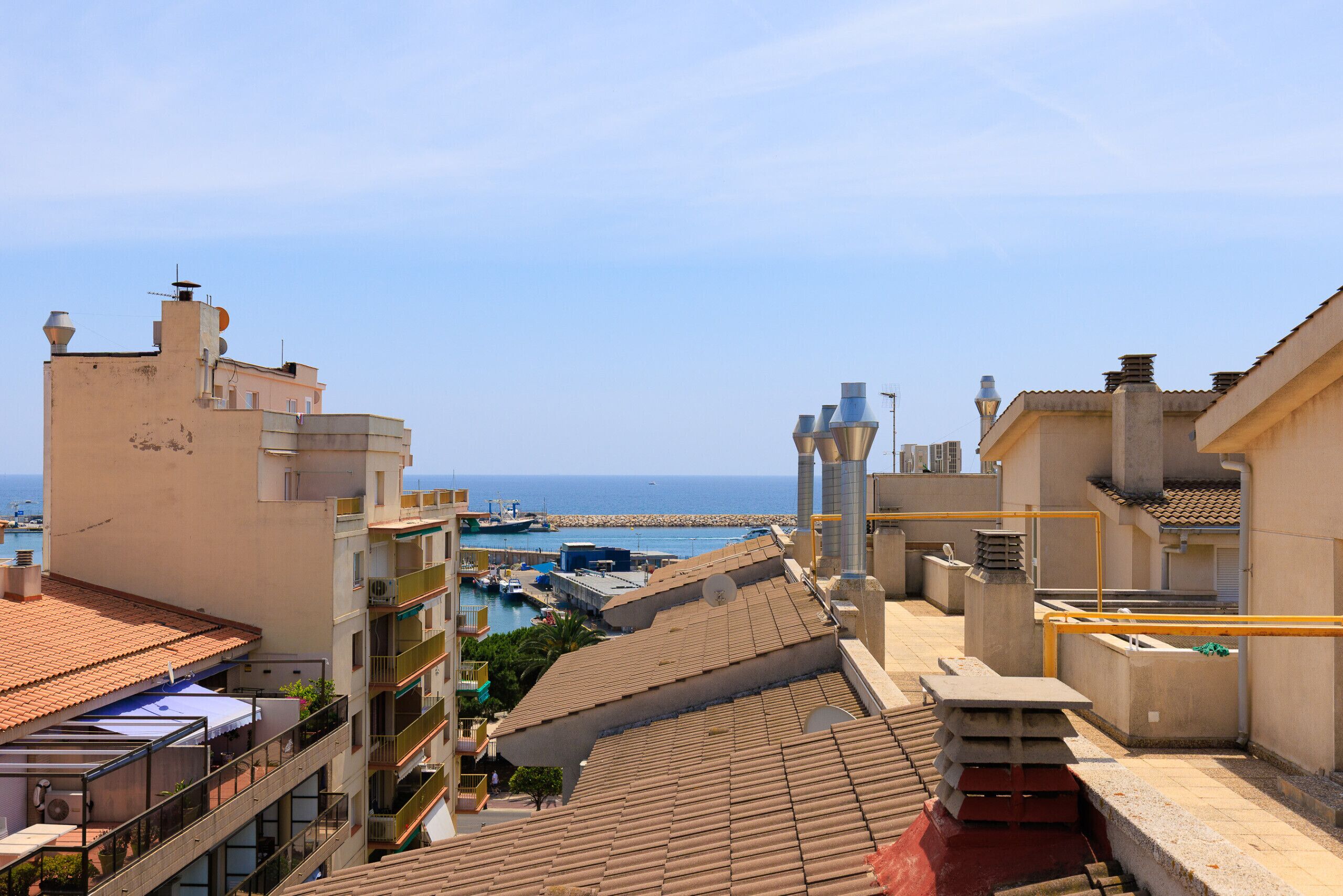Un hotel sul lungomare con numerosi balconi, vista mare e un porto turistico sullo sfondo.