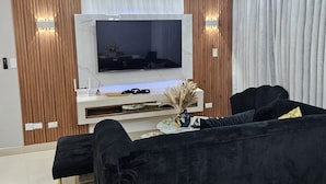 A modern living room with a large flat-screen TV, a black sofa, and a decorative vase.