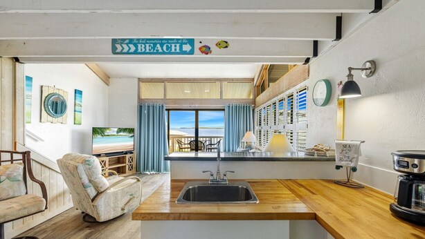 Une cuisine décorée sur le thème de la plage, avec vue sur l’océan, un coin repas offrant également une vue, et un panneau indiquant : « Les plus beaux souvenirs se créent à la PLAGE ».