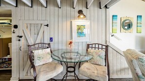 Une pièce avec un mur en bois rustique, une table en verre avec deux chaises, un tableau encadré et un petit vase décoratif.
