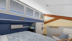 A bedroom with a bed, a TV, and a chair. - Loft style condo with balcony and king bed (Cedar Key)