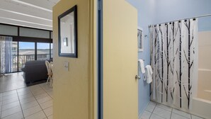A hotel room with a large window, a door with a mirror, and a bathroom with a tree-patterned shower curtain. - Loft style condo with balcony and king bed (Cedar Key)