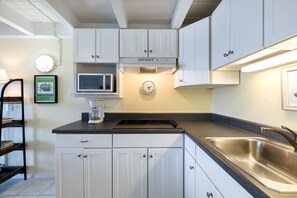 A kitchen with white cabinets, a microwave, a coffee maker, a clock, and a stainless steel sink. - Loft style condo with balcony and king bed (Cedar Key)