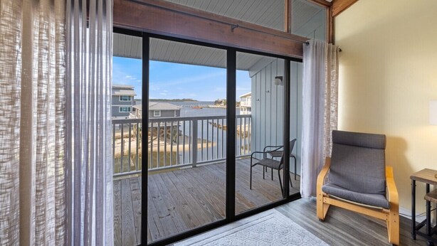 A room with a sliding glass door leading to a balcony with a wooden deck, a chair, and a small table. - Loft style condo with balcony and king bed (Cedar Key)