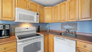 A compact kitchen with wooden cabinets, a microwave, a stove, a dishwasher, and a coffee maker.