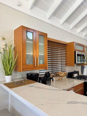 A modern kitchen with wooden cabinets, a stainless steel stove, and a large island with a marble countertop. - Bamboo Breeze 5-bedroom villa in Richmond Estate (Priory)