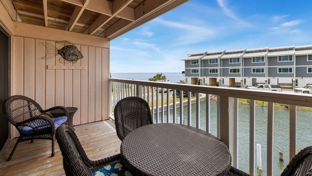 A balcony with wicker furniture, a view of a marina, and a multi-story building in the background. - Balcony 🌴 King Bed + Sofa Bed 🌴 Water Views (Cedar Key)