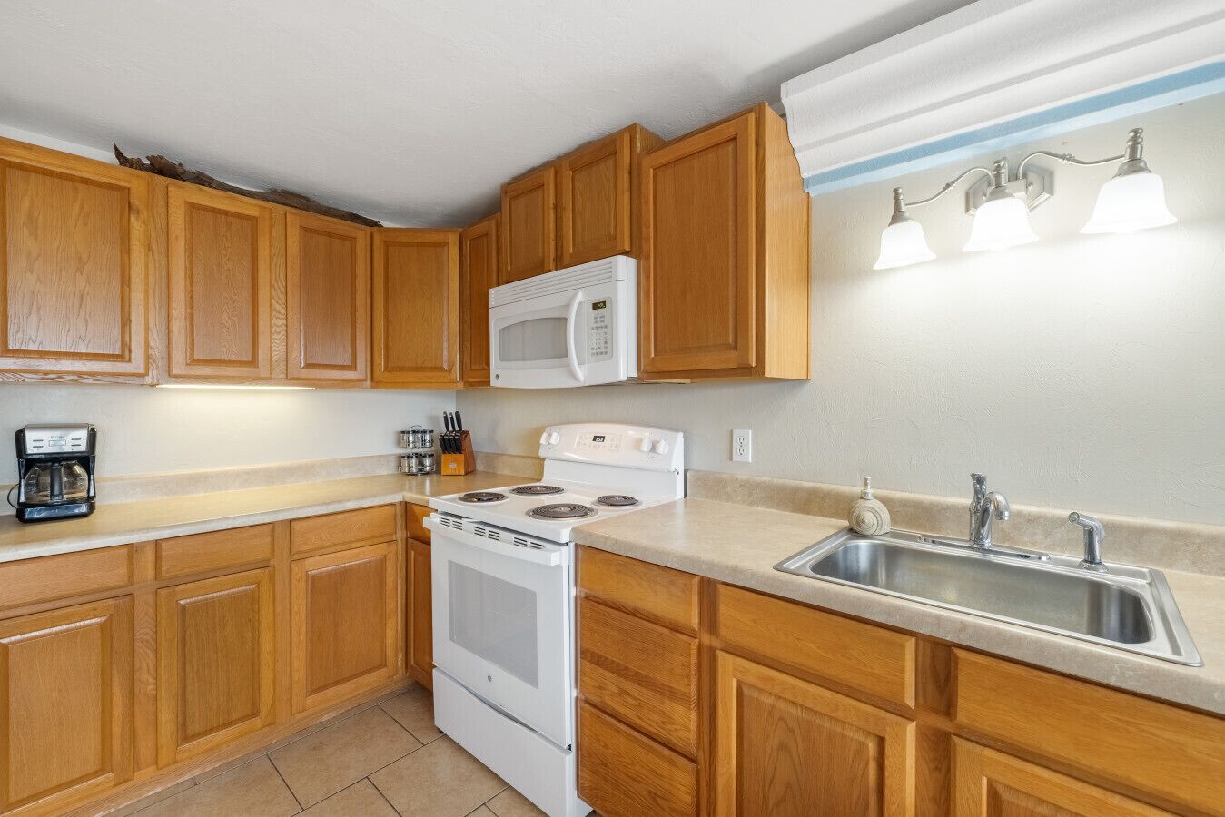 A kitchen with wooden cabinets, a white stove, a microwave, a sink, and a coffee maker.