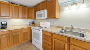 A kitchen with wooden cabinets, a white stove, a microwave, a sink, and a coffee maker. - Balcony 🌴 King Bed + Sofa Bed 🌴 Water Views (Cedar Key)