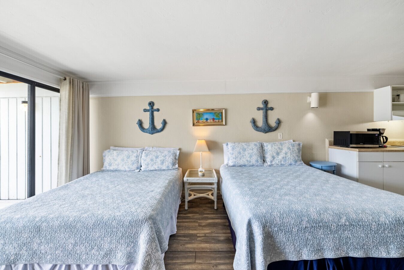 Ein Zimmer mit zwei Betten, einem kleinen Tisch, einer Lampe und einer Küchenzeile.