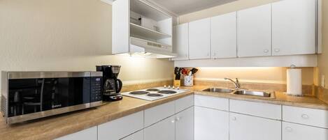 A compact kitchen with white cabinets, a built-in microwave, a coffee maker, and a sink.