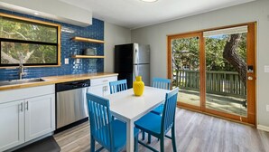 A modern kitchen with blue and white cabinetry, a built-in oven, and a dining area with blue chairs and a white table. - A Cozy Canopy Getaway in Cedar Key (Cedar Key)