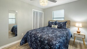 A bedroom with a bed, a ceiling fan, a nightstand with a lamp, and a window with blinds. - A Cozy Canopy Getaway in Cedar Key (Cedar Key)