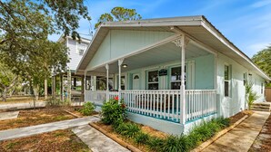 A light blue house with a porch, surrounded by a garden with various plants and a pathway leading to the entrance.