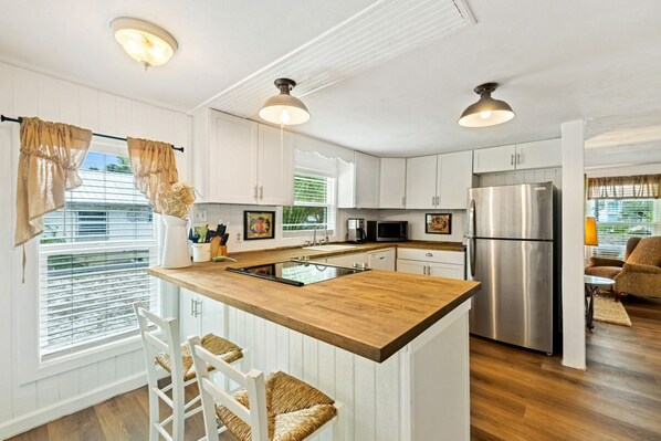 A modern kitchen with white cabinetry, a wooden island, stainless steel appliances, and pendant lighting. - Historic cottage in quiet neighborhood (Cedar Key)