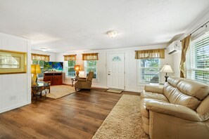 A spacious living room with a leather sofa, a dining area with a table and chairs, and a kitchen area with a refrigerator and a window. - Historic cottage in quiet neighborhood (Cedar Key)