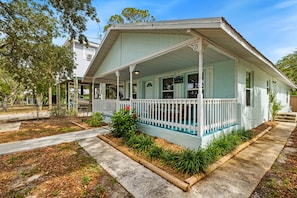 A light blue house with a porch, surrounded by a garden with various plants and a pathway leading to the entrance. - Historic cottage in quiet neighborhood (Cedar Key)