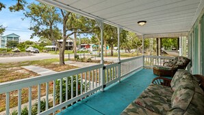 A covered porch with a blue floor, white railing, and wicker furniture.