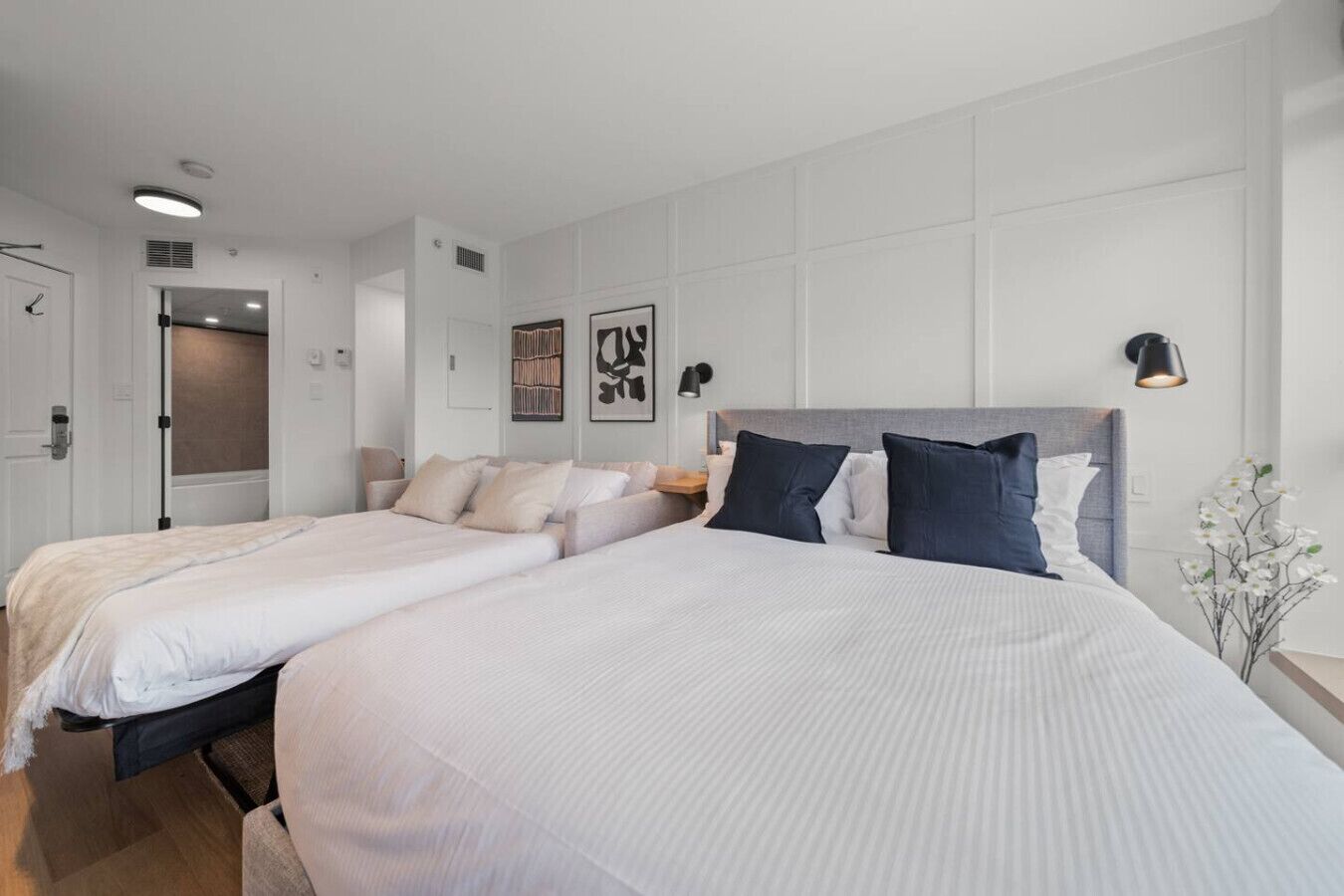 Een hotelkamer met twee bedden, een nachtkastje, een lamp en een kunstwerk aan de muur.