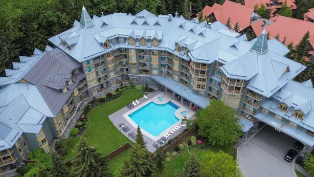 A large hotel with a central swimming pool, surrounded by lush greenery and multiple balconies.