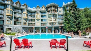 A hotel with a large pool, red chairs, and a stone facade.