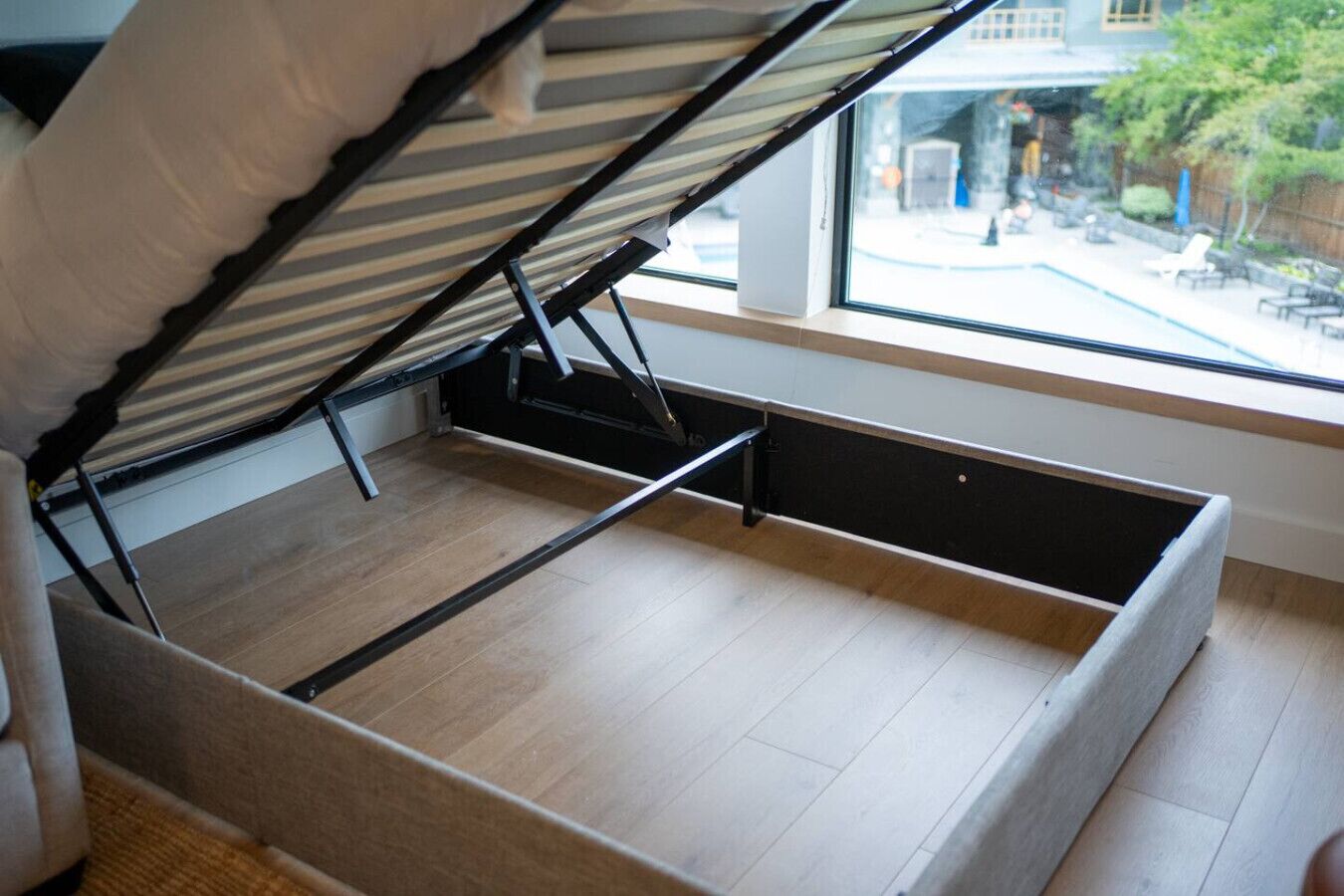 A room with a bed that can be converted into a sofa, a window with a view of the outside, and a wooden floor.