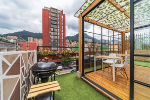 Un balcon doté d’une terrasse en bois, d’un barbecue et d’une table avec des chaises.