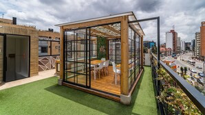 A modern glass-walled room with a wooden floor and white chairs, overlooking a city street. - |Ahead| Spacious 3BR @Chapinero with Co-working (Bogotá)