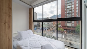 A bedroom with a large window, a bed, and a view of a busy street and buildings. - |Ahead| Spacious 3BR @Chapinero with Co-working (Bogotá)
