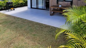 Een moderne tweelaags woning met een overdekte patio, een barbecuegrill en een houten bank.