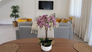 Een moderne woonkamer met een eettafel, banken en een aan de muur bevestigde televisie.