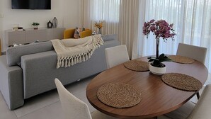 Een moderne woonkamer met een grijze bank, een houten eettafel met geweven placemats en een plafondventilator.