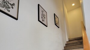 Een houten trap met een leuning, die leidt naar een plateau met drie ingelijste botanische prints aan de muur.