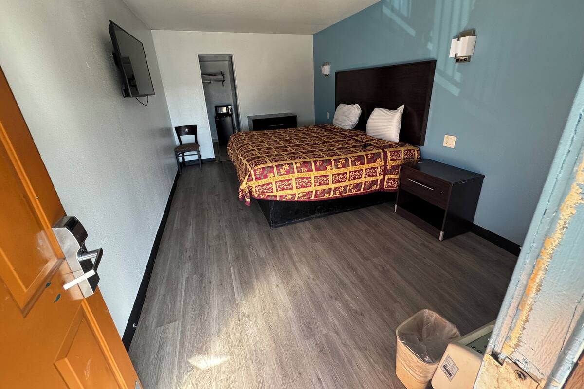 Una habitación de hotel con cama, mesita de noche y televisión montada en la pared.