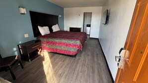 A hotel room with a bed, a desk, a chair, a wardrobe, and a door. - spanish trails inn (Lancaster)