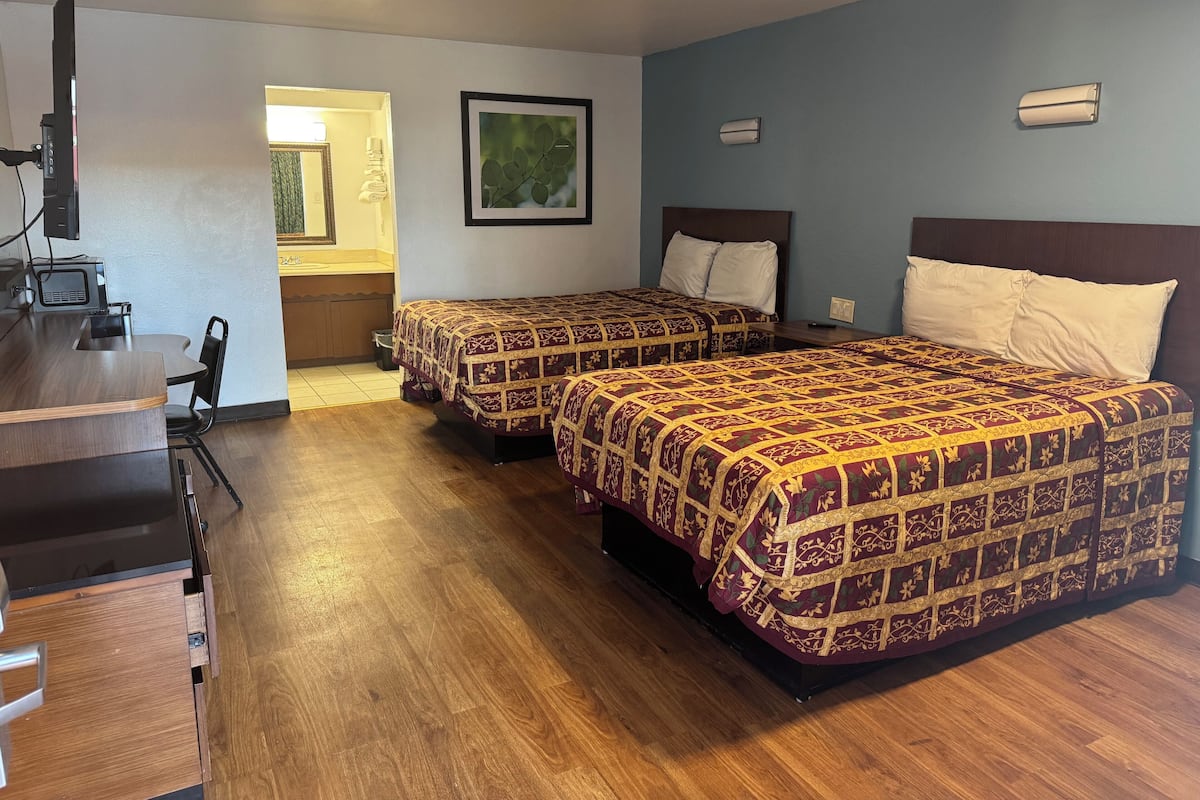 Habitación de hotel con dos camas, un escritorio, una silla y una pequeña kitchenette.