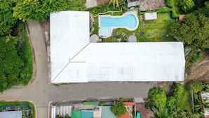 Une vue aérienne d’un bâtiment doté d’une piscine, entouré de verdure et situé à proximité d’une route.