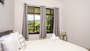 Une chambre d’hôtel avec un grand lit, des rideaux gris, une vue sur la verdure et une petite table avec des serviettes.